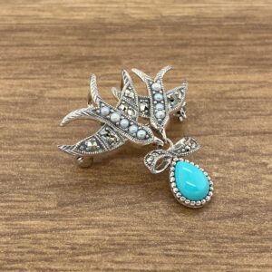 A silver brooch with turquoise and pearls on a wooden table.
