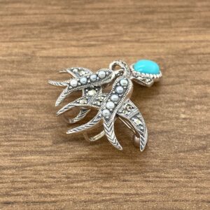 A silver brooch with turquoise and pearls on a wooden table.