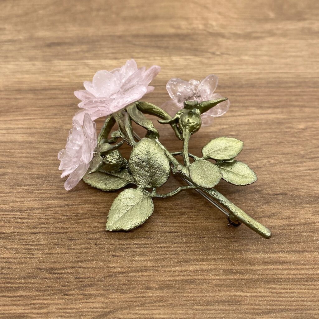 A pink rose brooch on a wooden table.