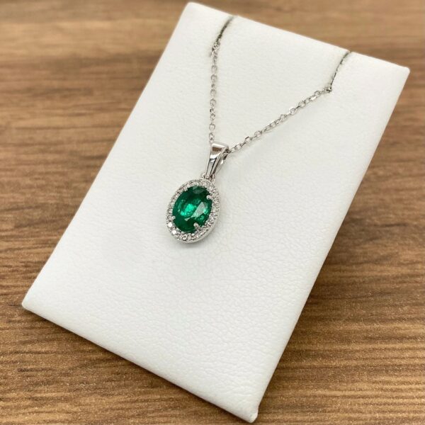 An emerald and diamond pendant on a white background.