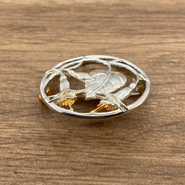 Silver and gold circular brooch with leaf design.