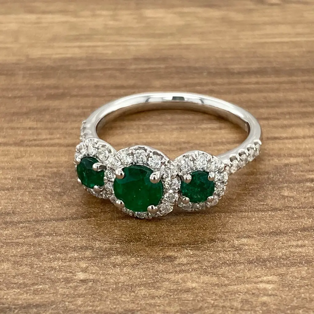 Emerald and diamond halo ring on wood.