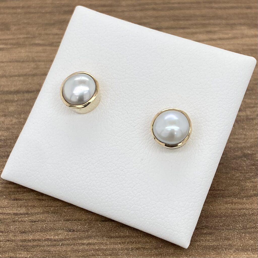A pair of white pearl stud earrings on a white background.