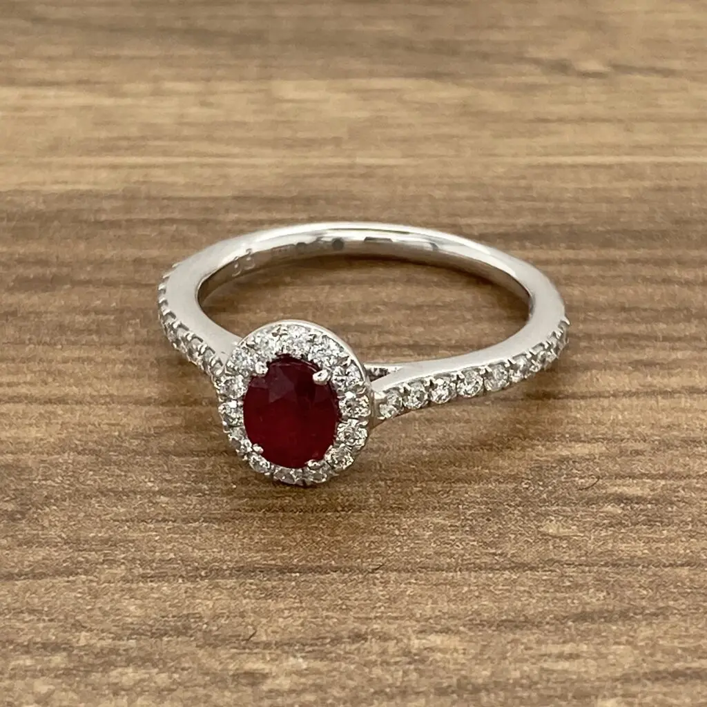 An oval ruby and diamond ring on a wooden table.