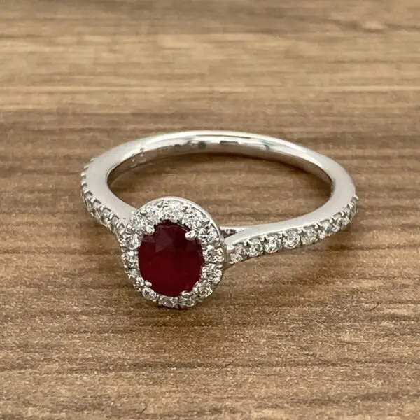 An oval ruby and diamond ring on a wooden table.