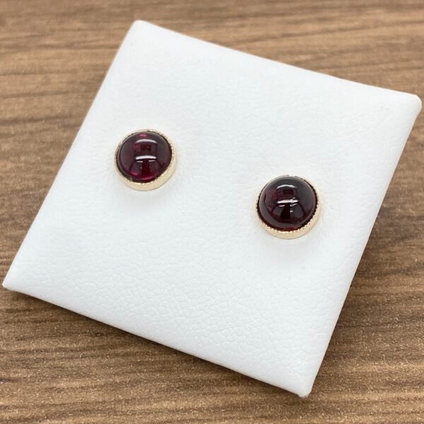 A pair of garnet stud earrings on a white table.