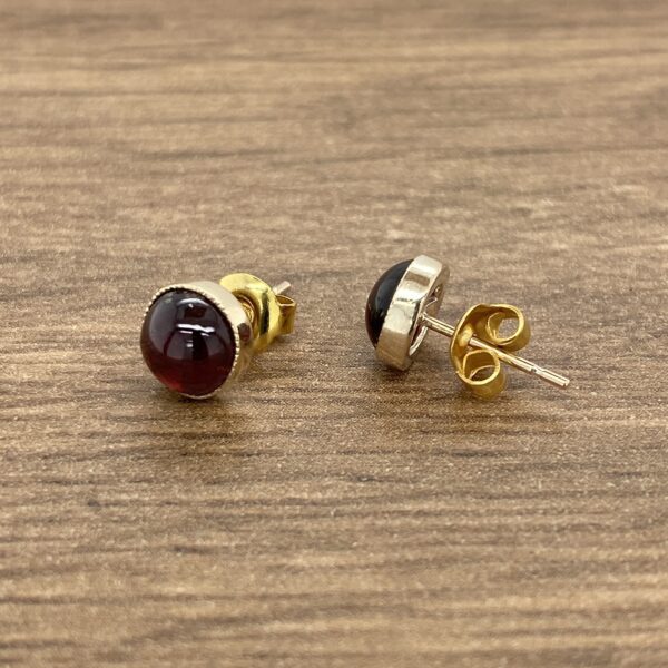 Gold earrings with red gemstone studs.