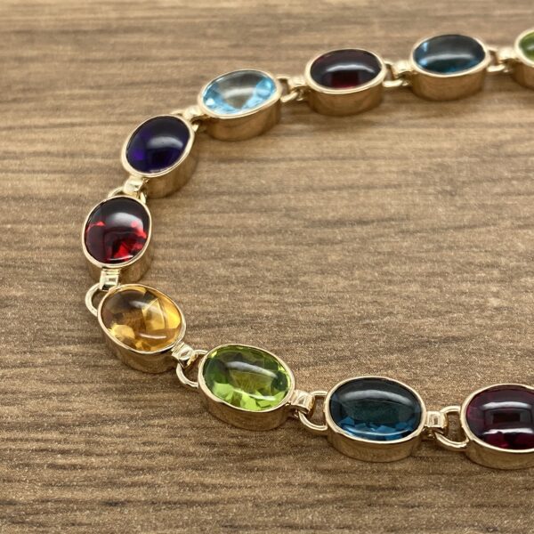 A Multigem Collet Set Bracelet with multi colored stones on a wooden table.