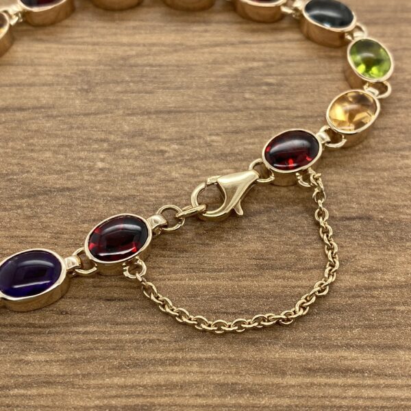 A Multigem Collet Set Bracelet with multi colored stones on a wooden table.