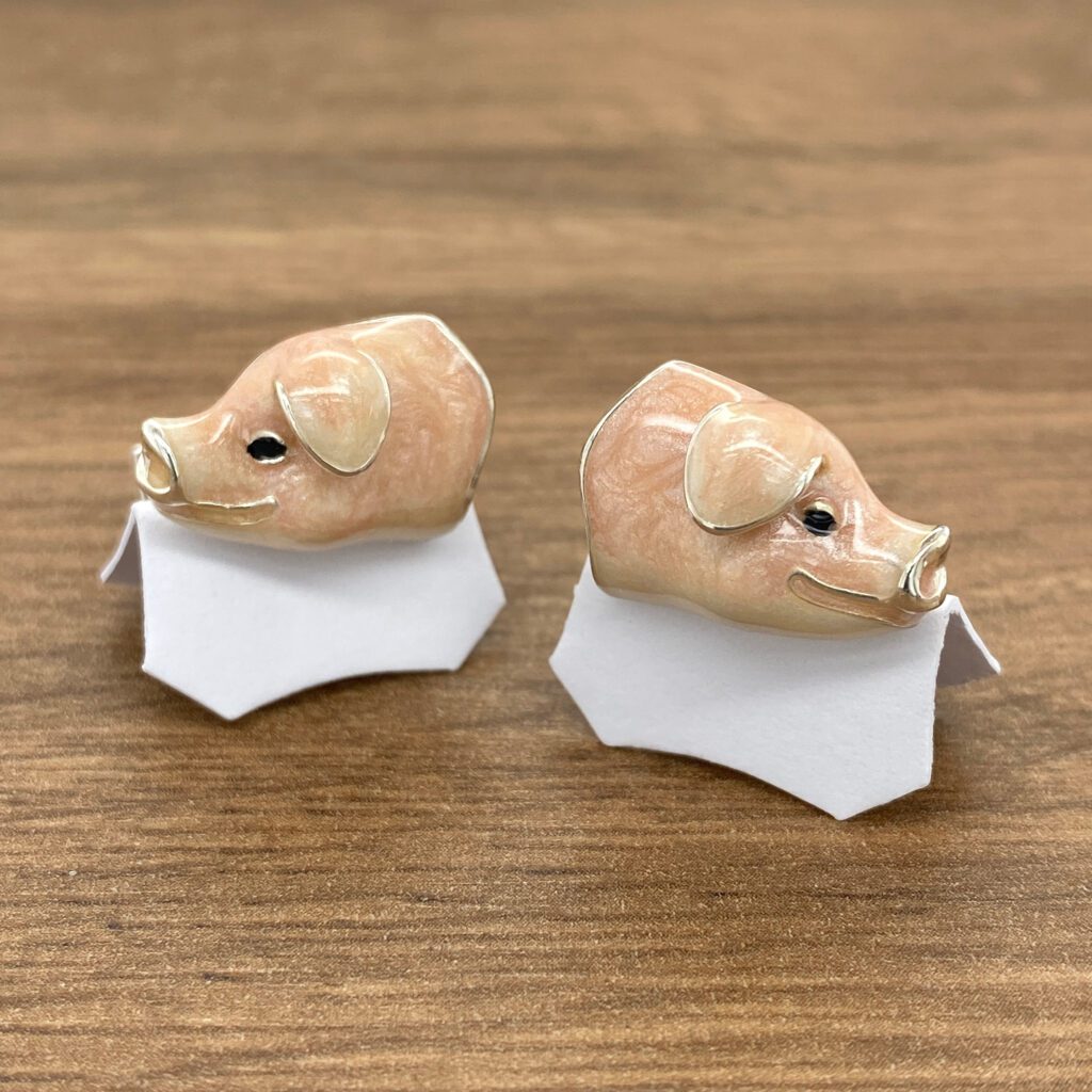 Two pig shaped cufflinks on a wooden table.