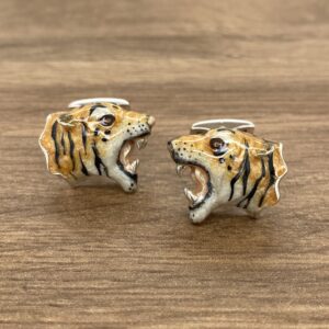 A pair of tiger cufflinks on a wooden table.
