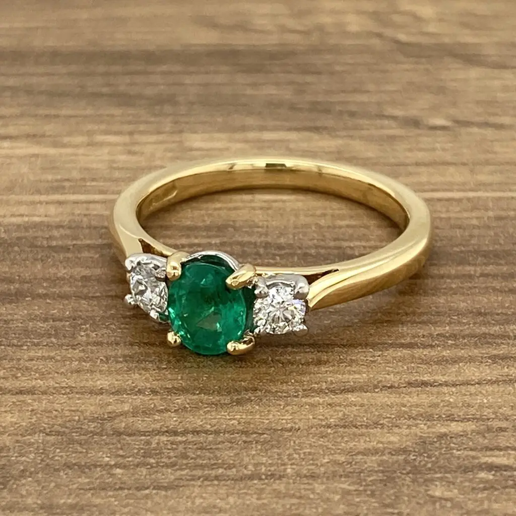 An oval emerald and diamond ring on a wooden table.