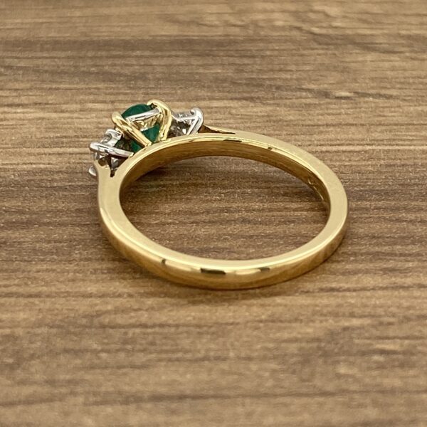 An emerald and diamond ring on a wooden table.