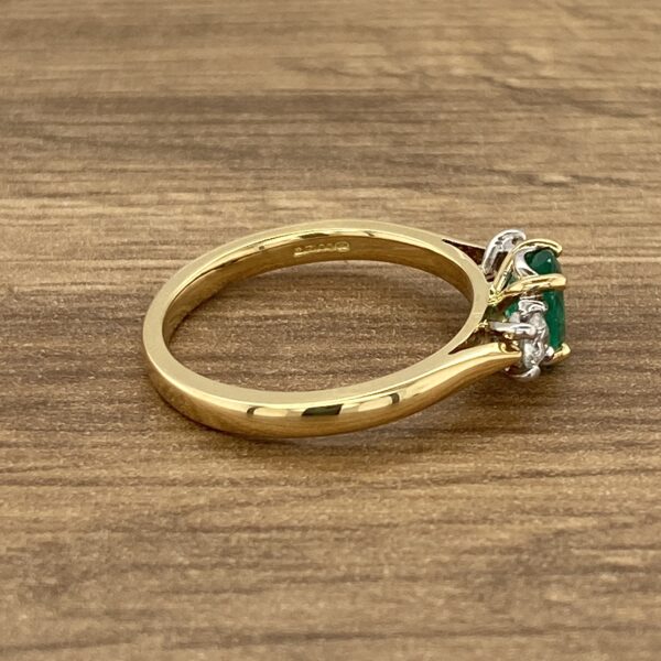 An emerald and diamond ring on a wooden table.