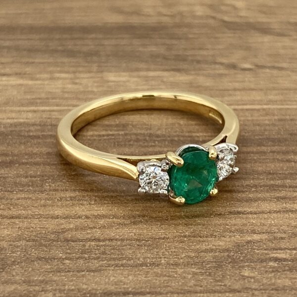 An emerald and diamond ring on a wooden table.