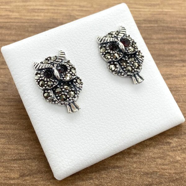 Pair of silver owl earrings with red eyes.