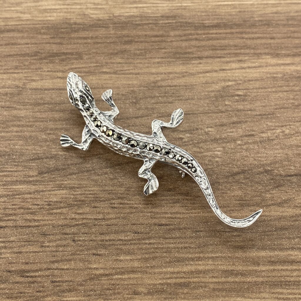 Silver lizard brooch on wood background.