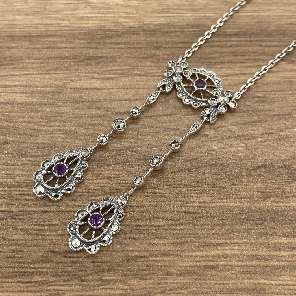 A silver necklace with purple stones on it.