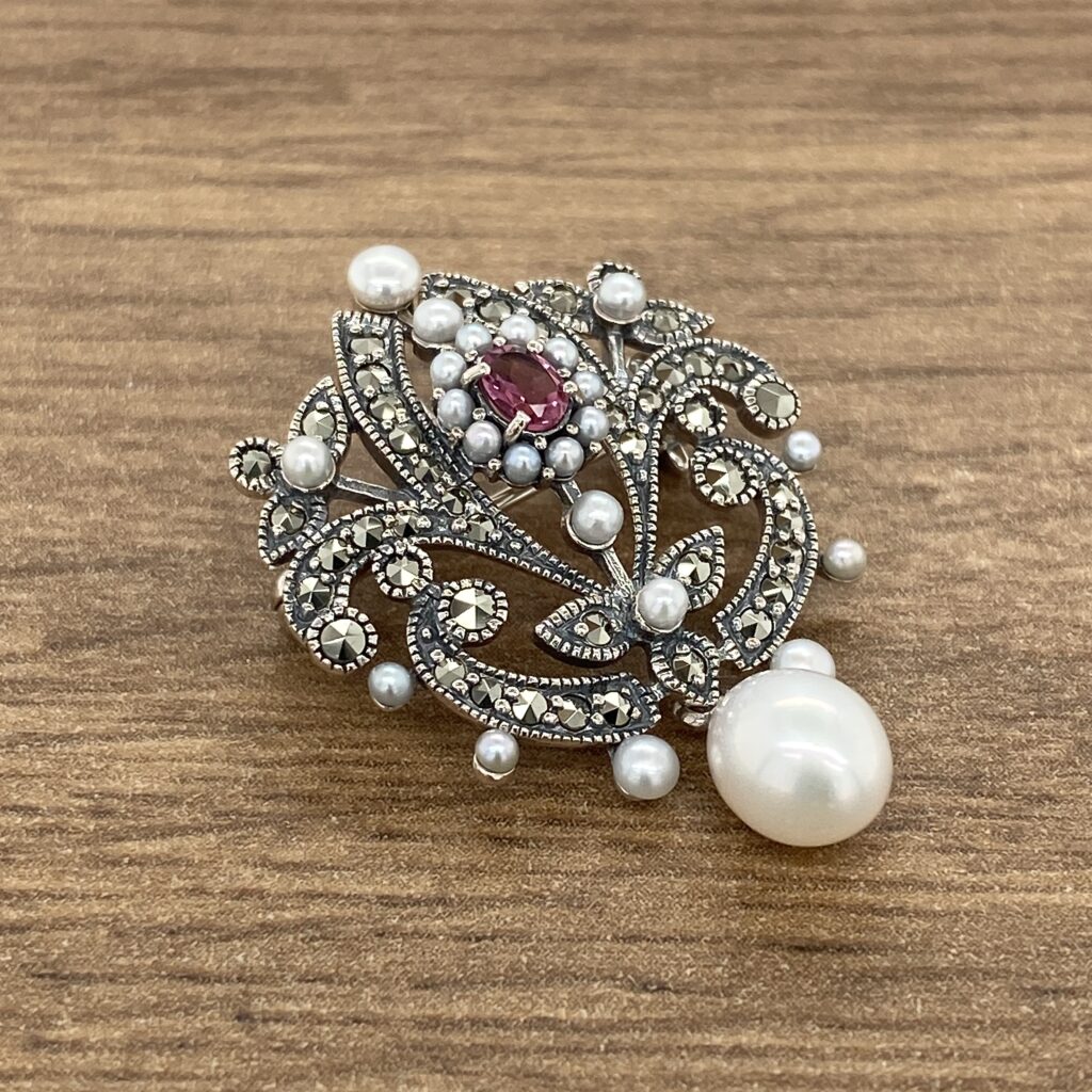 A pearl and ruby broochle on a wooden table.