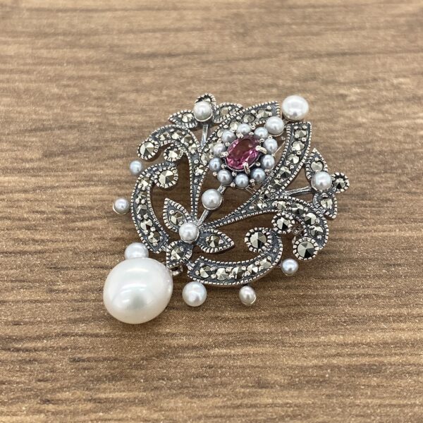 A pearl and ruby broochle on a wooden table.