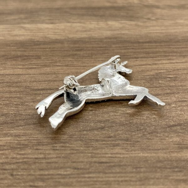 A silver unicorn brooch on a wooden table.