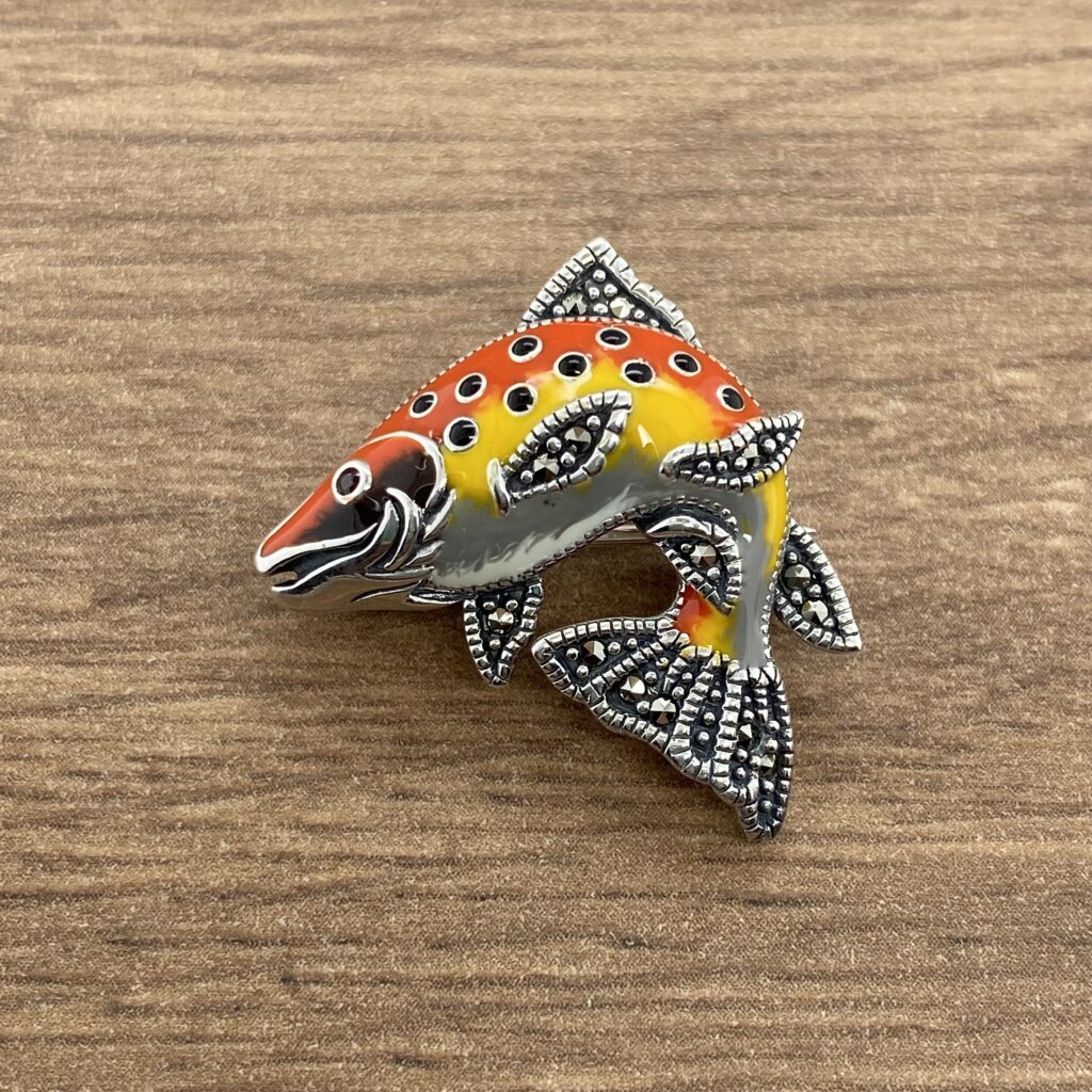 A colorful fish brooch on a wooden table.
