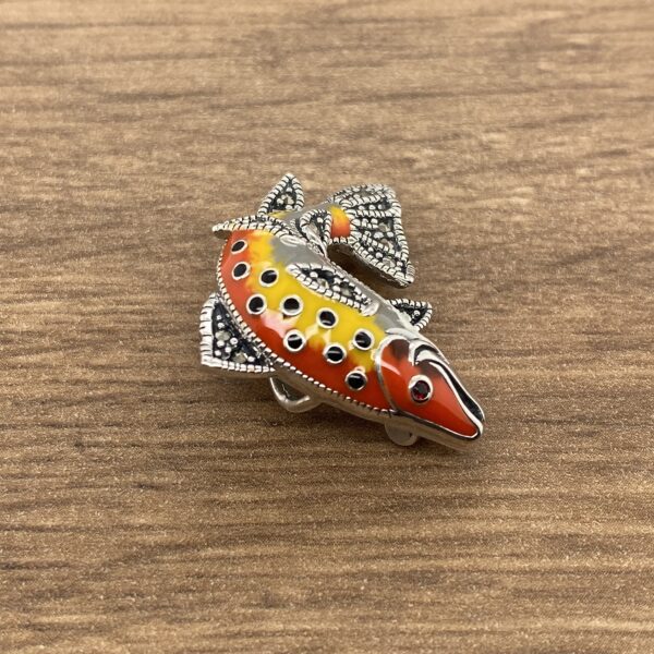 A colorful fish brooch on a wooden table.