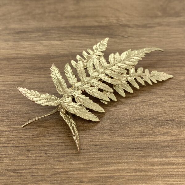 A gold fern leaf brooch on a wooden table.