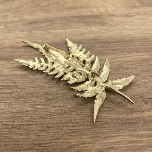 A gold fern leaf brooch on a wooden table.