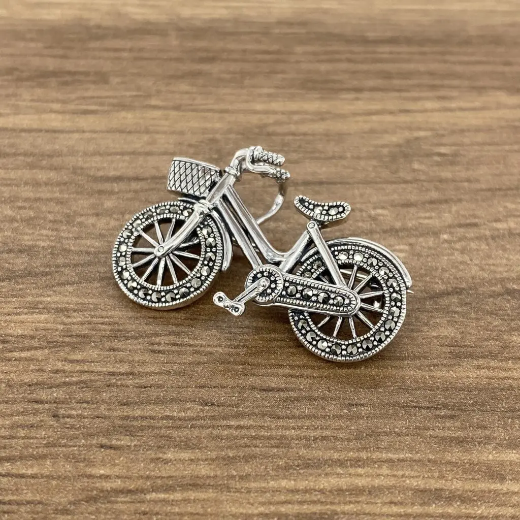 A silver bicycle brooch on a wooden table.