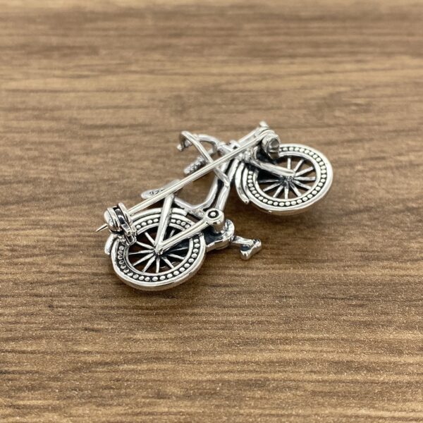 Silver bicycle brooch on wood background.