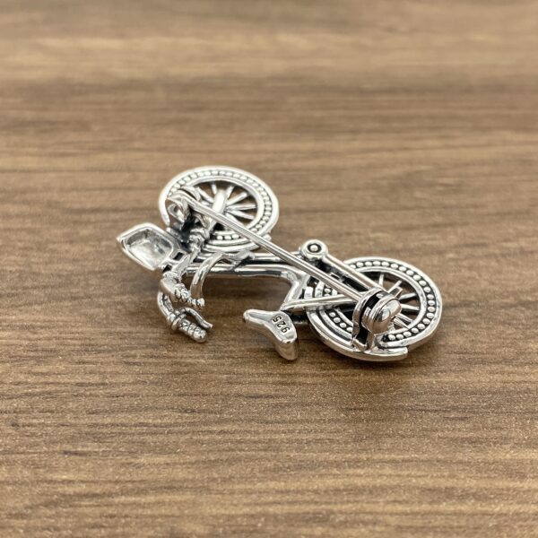 Silver bicycle brooch on wood background.