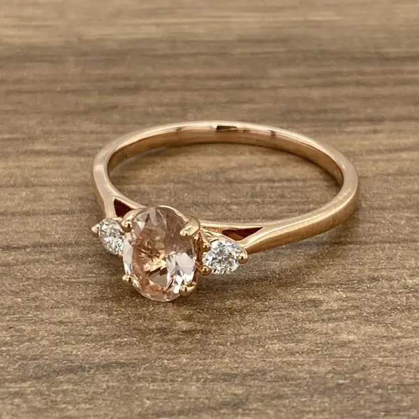 A rose gold ring with a morganite and diamonds on a wooden background.