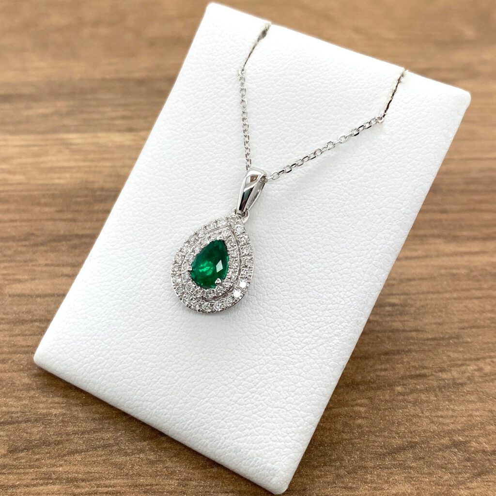 An emerald and diamond pendant on a white background.