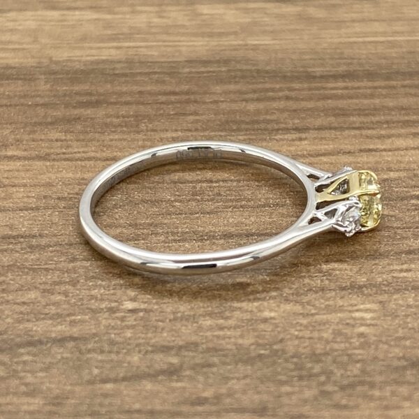 A yellow sapphire and diamond engagement ring on a wooden table.