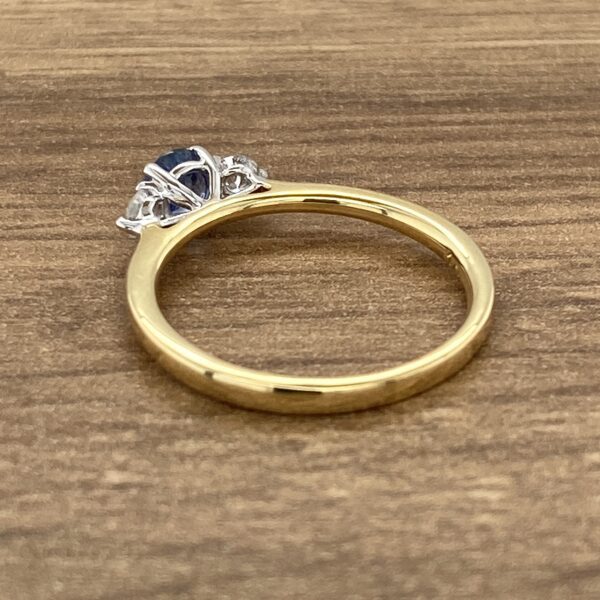 A sapphire and diamond engagement ring on a wooden table.