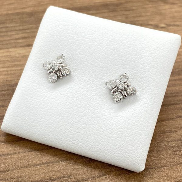 A pair of white gold diamond stud earrings on a wooden table.