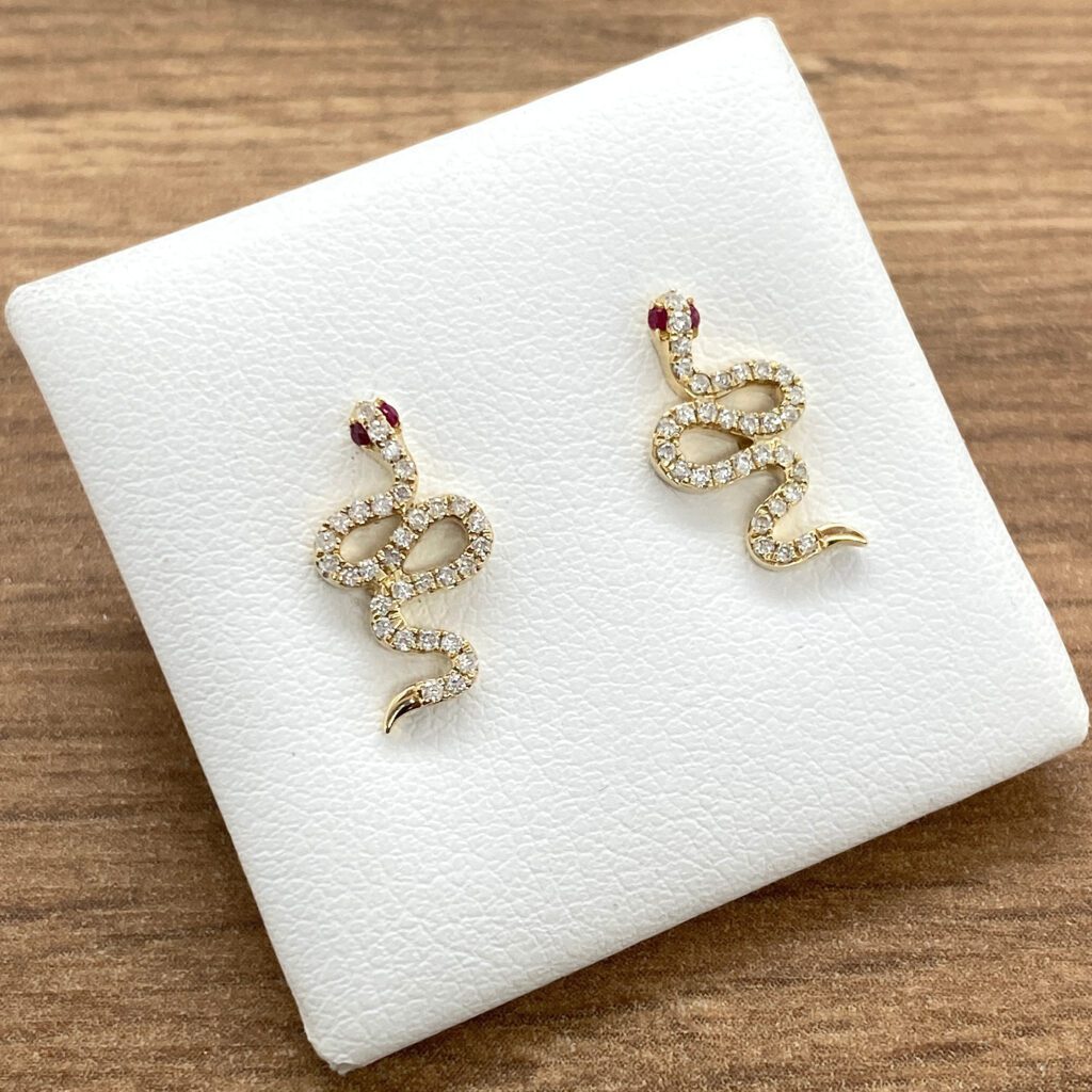 A pair of gold snake stud earrings with ruby stones.