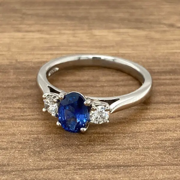 An oval sapphire and diamond ring on a wooden table.