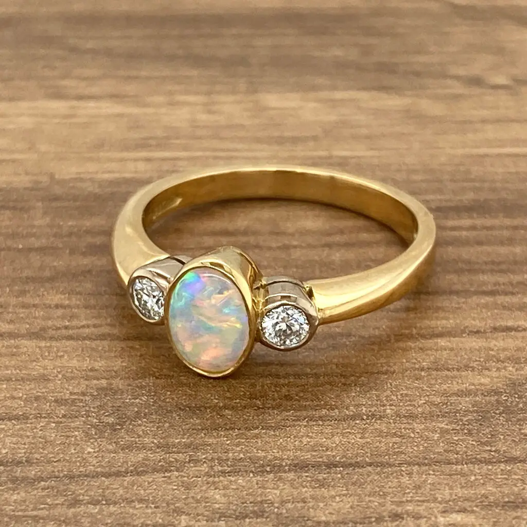 An opal and diamond ring on a wooden table.