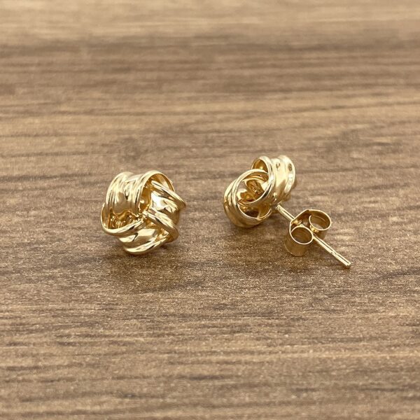 Gold knot stud earrings on wood background.