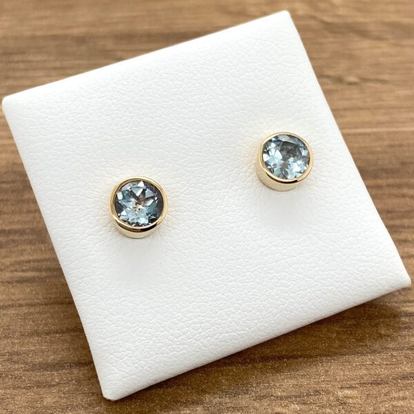 A pair of gold stud earrings with blue topaz stones.