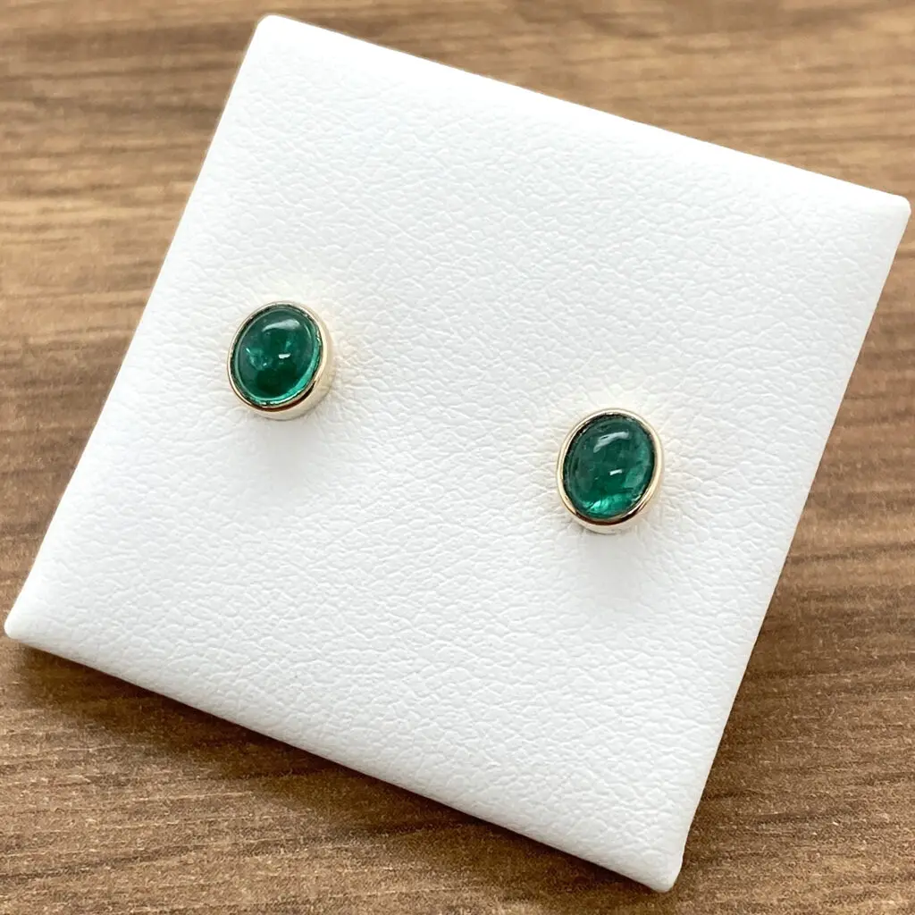 A pair of emerald stud earrings on a white background.