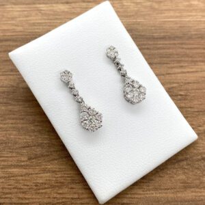 A pair of diamond drop earrings on a white table.