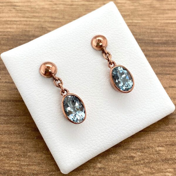 A pair of blue topaz and rose gold earrings.