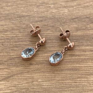 A pair of blue topaz and rose gold earrings.