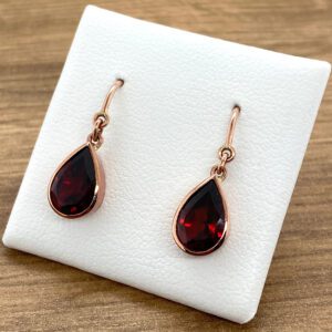 A pair of rose gold earrings with a garnet stone.