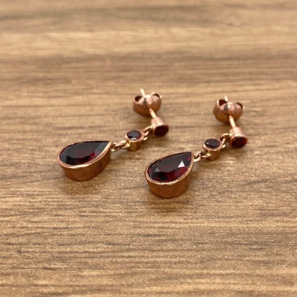 Rose gold earrings with red teardrop gems.