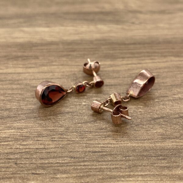 Rose gold earrings with red gemstone drops.