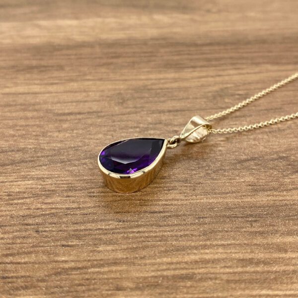 Gold necklace with purple gemstone pendant.